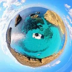 Little-planet daylight view of swimmers in the water all around an anchored yacht