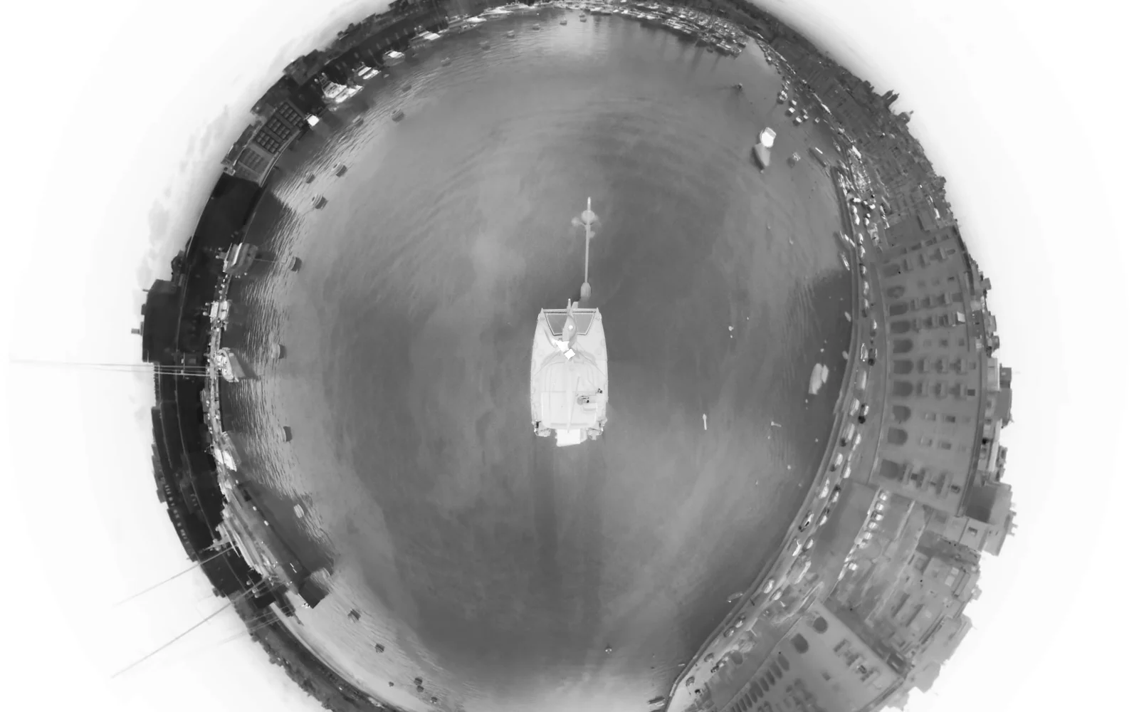 Thermal infrared footage of a harbour, seen as a complete 360° little-planet view in white-hot false colour: the vessel's deck at the centre, warm stone waterfront buildings and moored boats reading pale against cool dark water.
